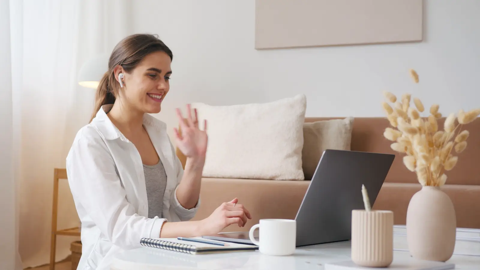 A woman waving and smiling at her laptop