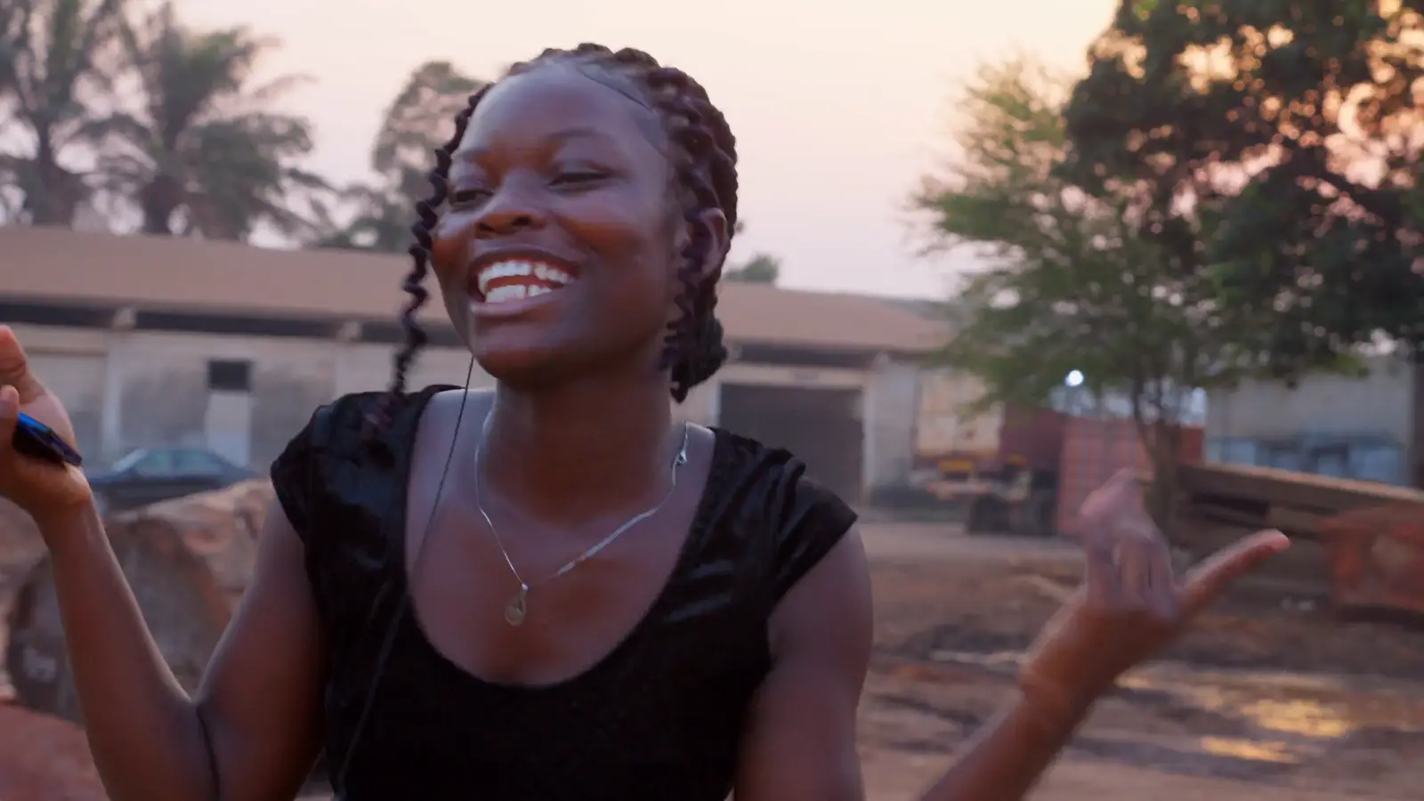 A young woman with earphones smiling outdoors at dusk