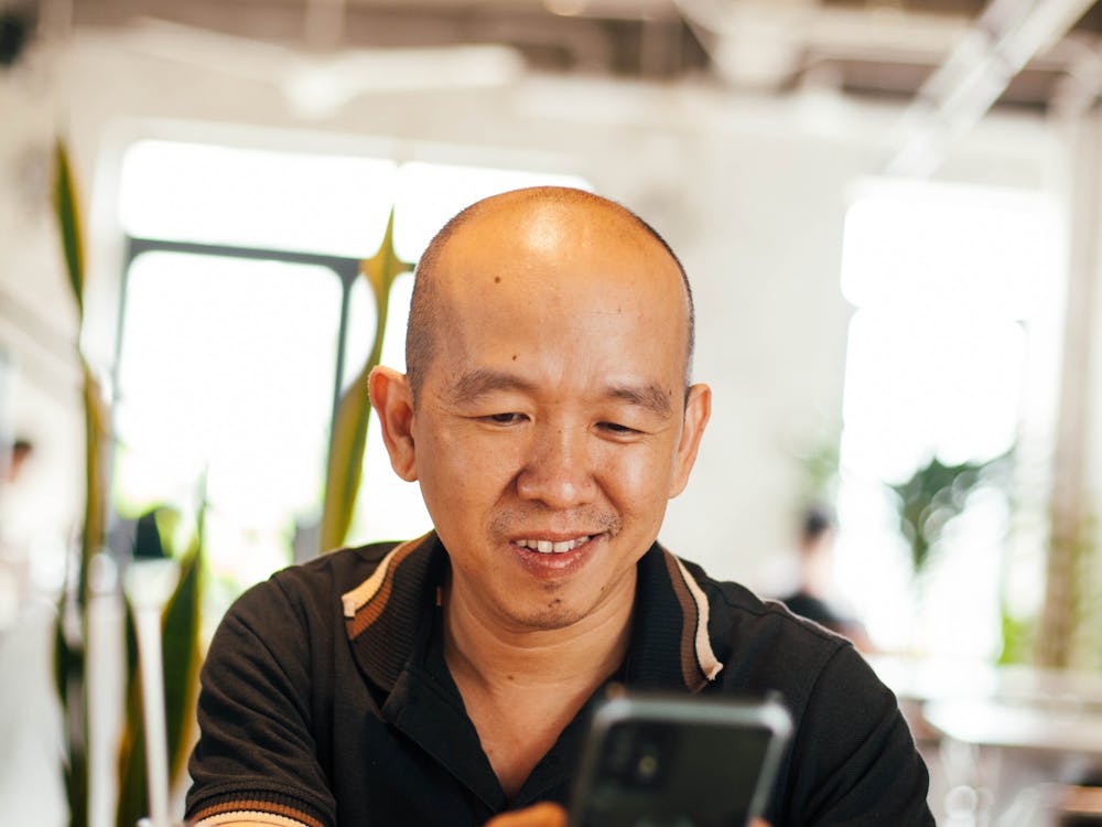 A man smiling at his phone over an iced coffee in a bright café.