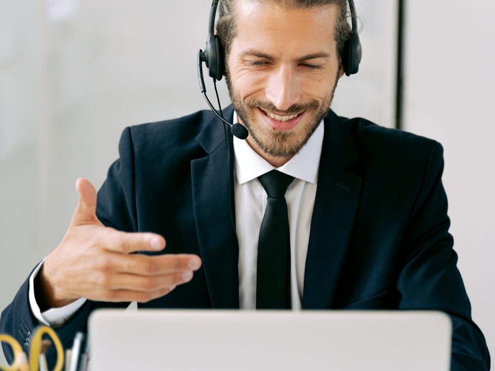 A man in a suit and headset talking and gesturing during a video call.