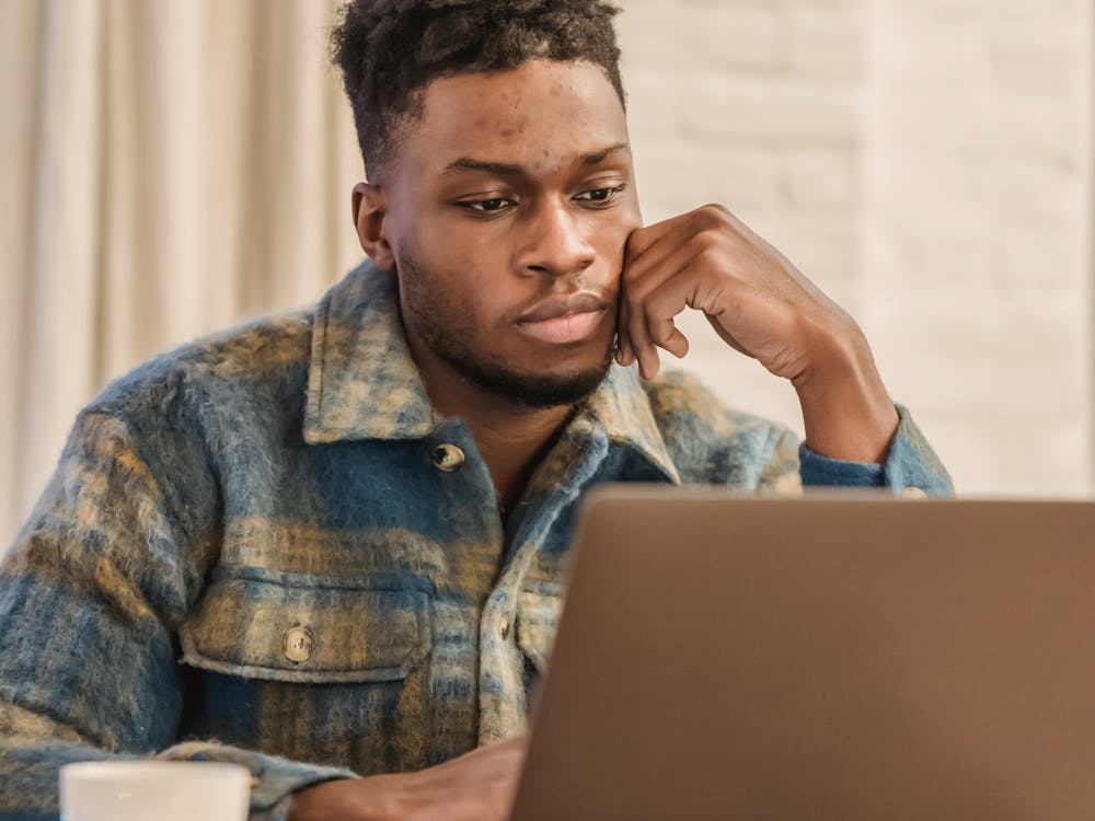 A close-up of a man looking thoughtfully at his laptop screen.