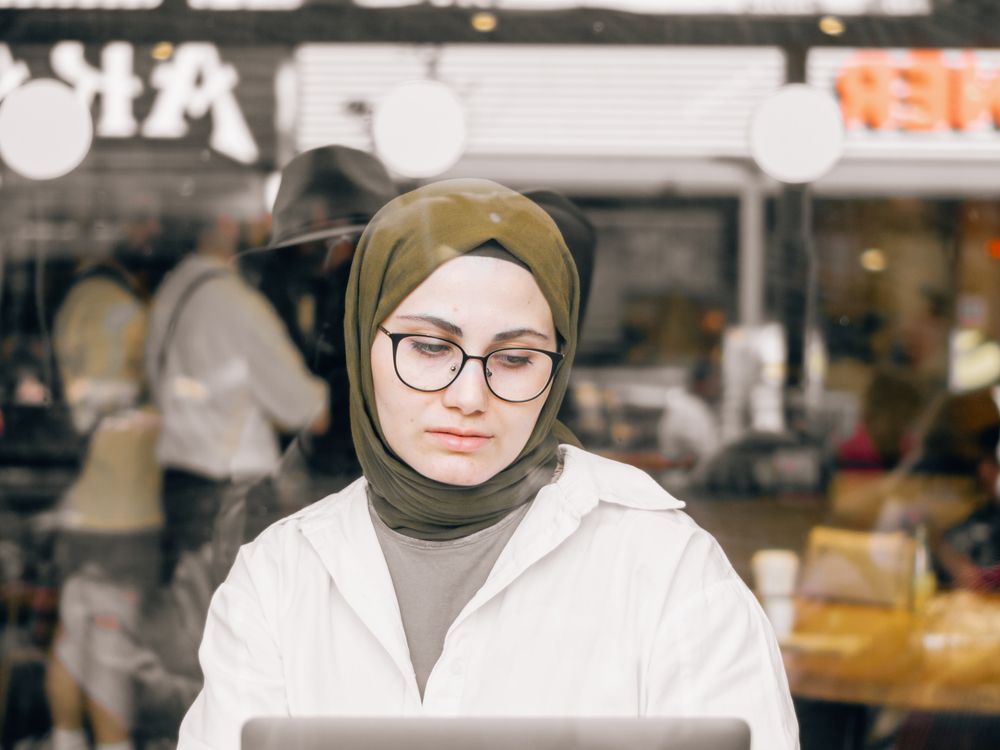 A woman working on her laptop at a busy street-side café, focused on the screen.