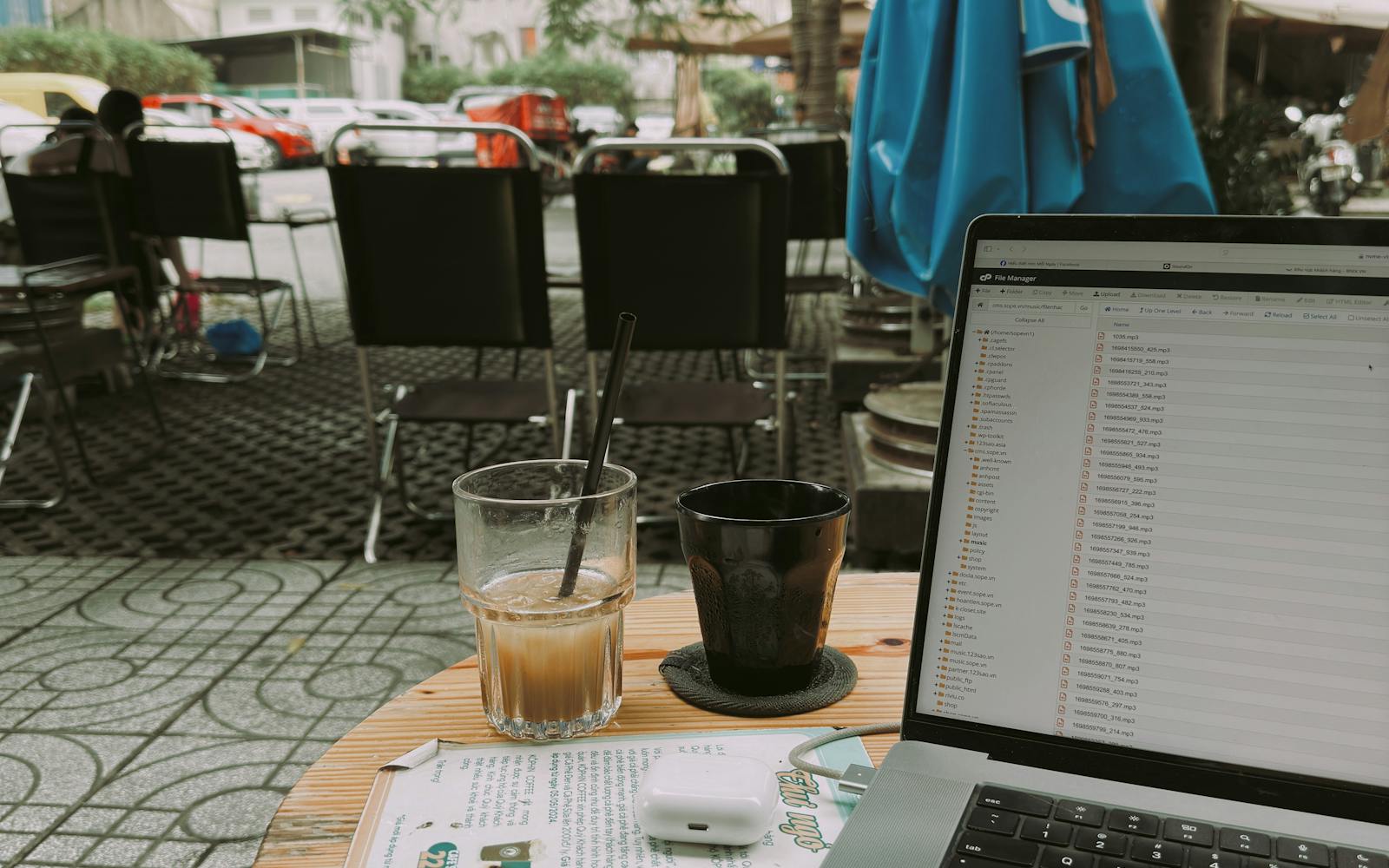 A laptop and an iced coffee on a table at an outdoor street café, the kind of place a digital nomad works from.