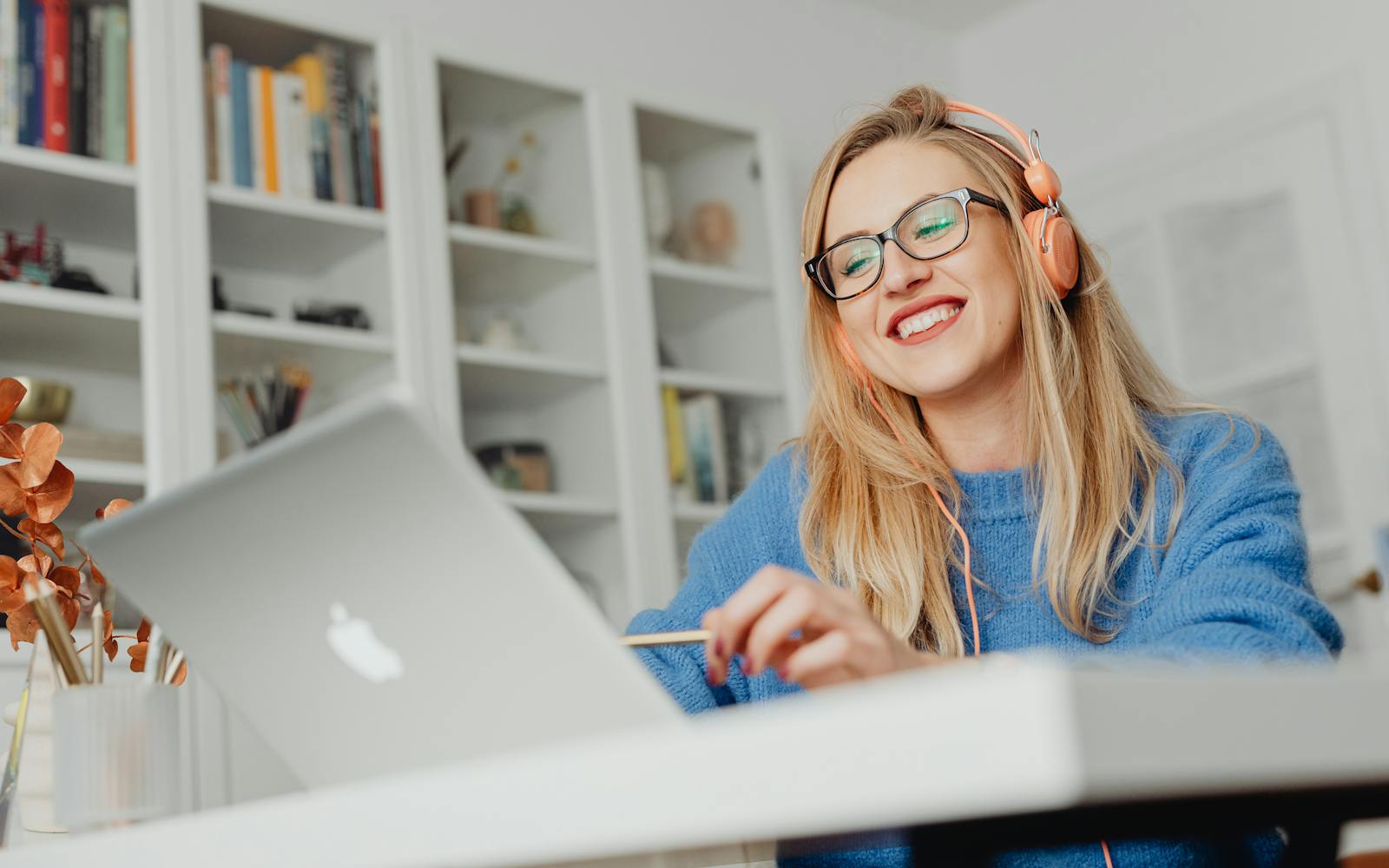 A woman in headphones smiling broadly at her laptop in a bright home office.