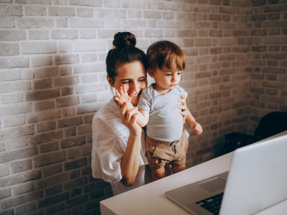 A mother and toddler waving at a laptop during a video call.