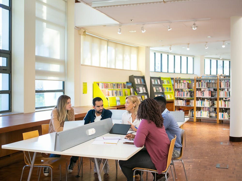 A group of students working together at a table in a bright university library.