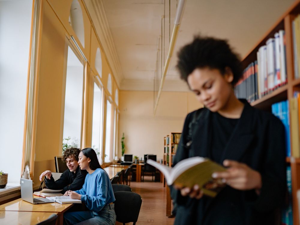 Students studying at a desk by the window of a university library.
