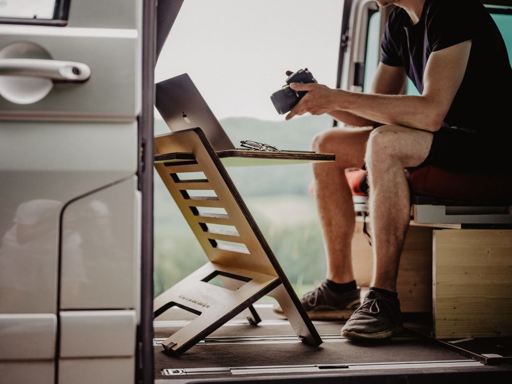 A laptop set up in the open doorway of a camper van looking out over green hills.