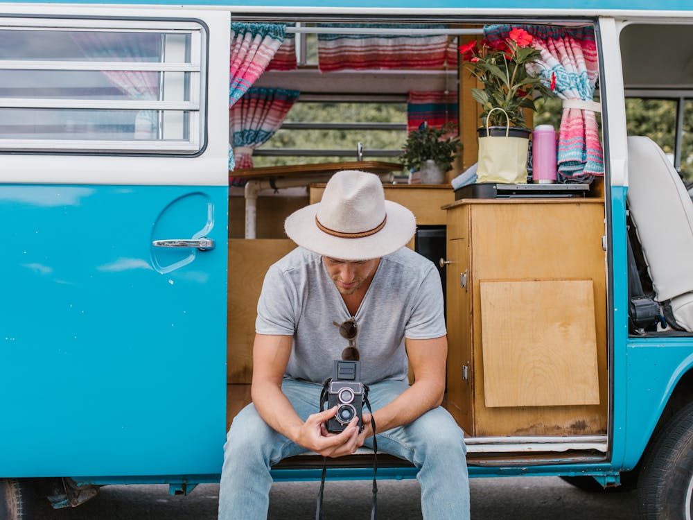 A man in a hat sitting in the doorway of a classic blue camper van.